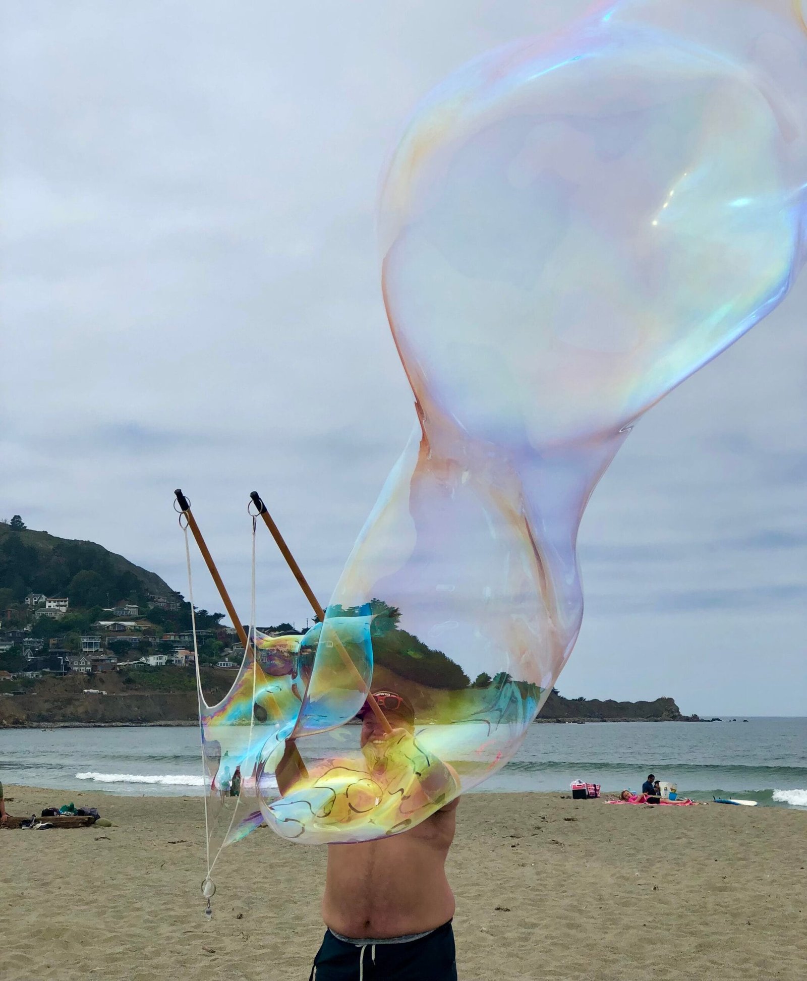Image features Quest House Director Owen standing on a beach and creating giant bubbles.
