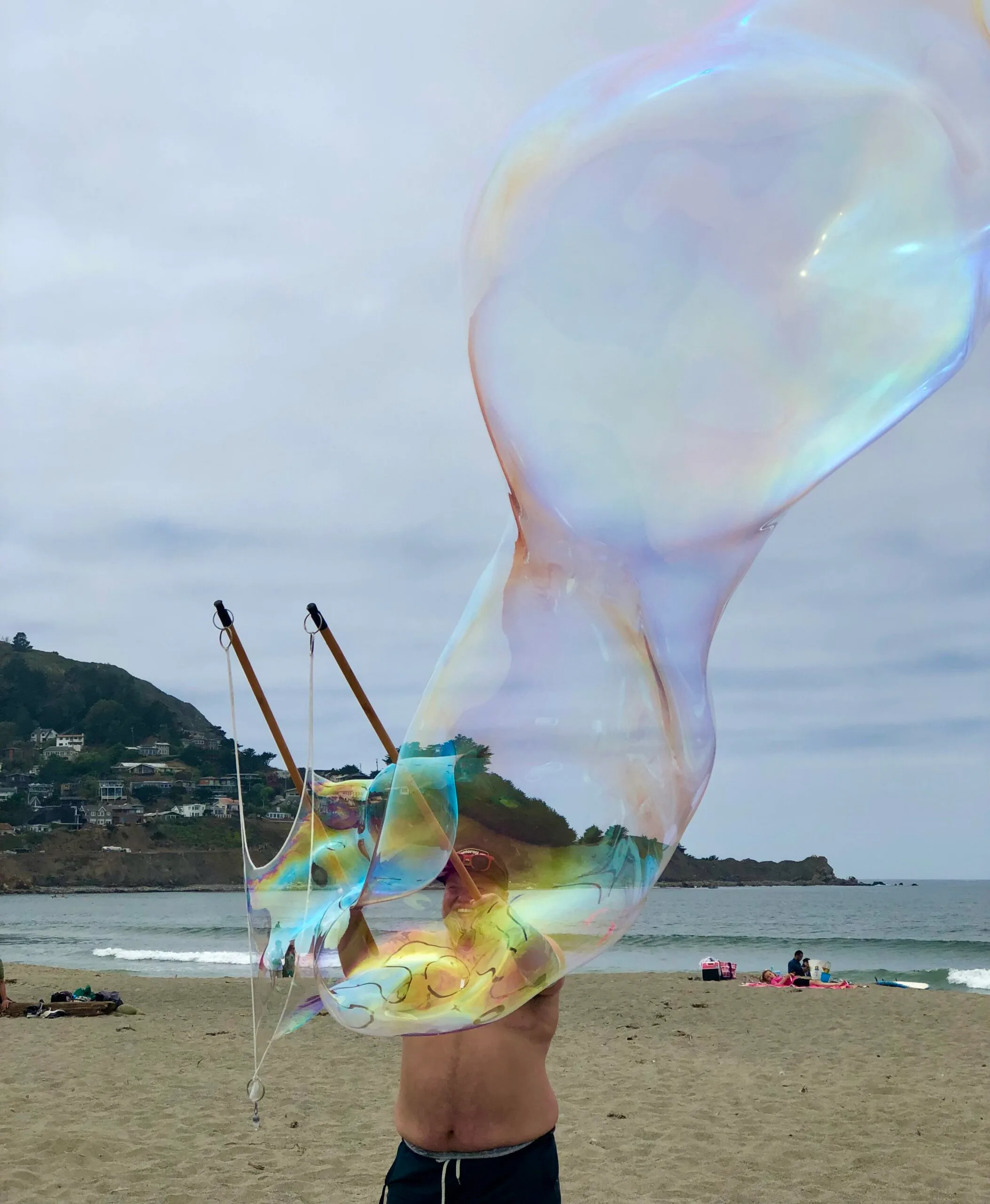 Image features Quest House Director Owen standing on a beach and creating giant bubbles.
