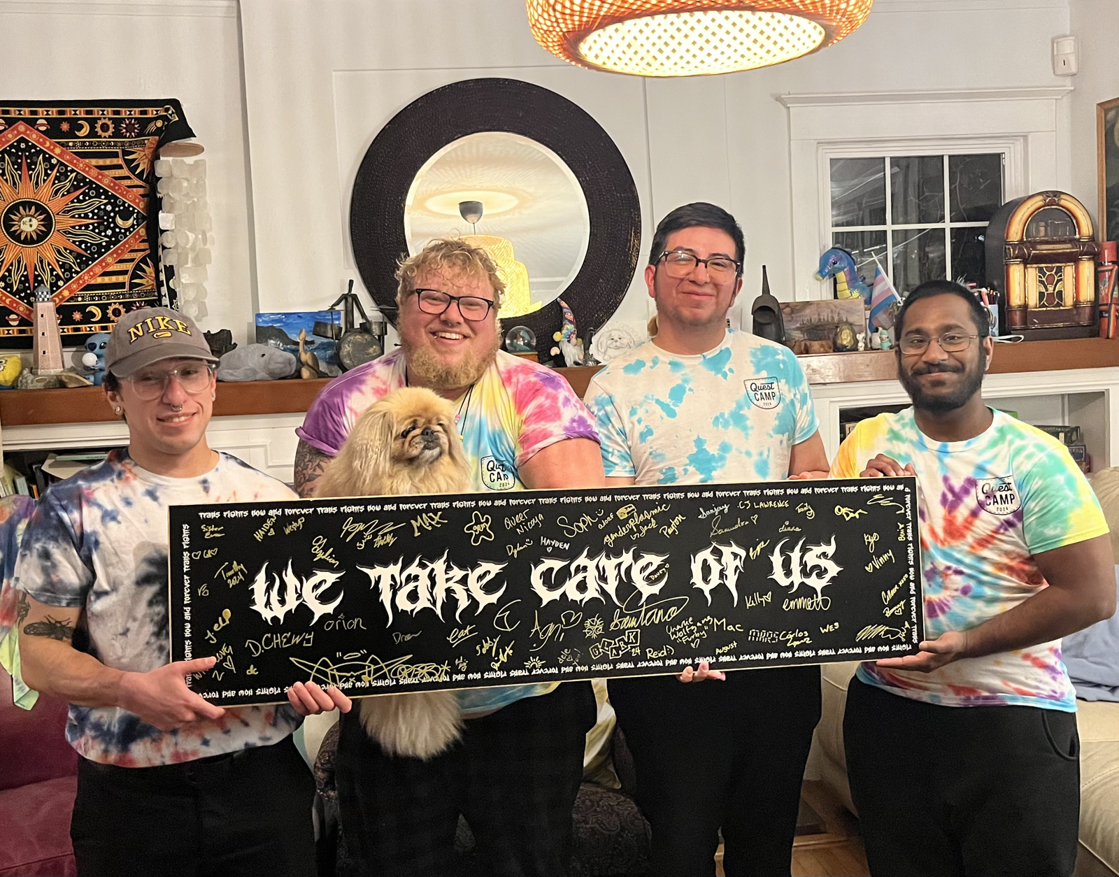 Image featuring some of Quest House's Volunteers holding a sign that says "We take care of us". The sign features dozens of signatures.